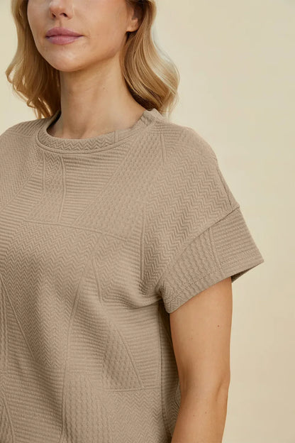 Woman wearing a textured beige short sleeve knit top with crew neckline
