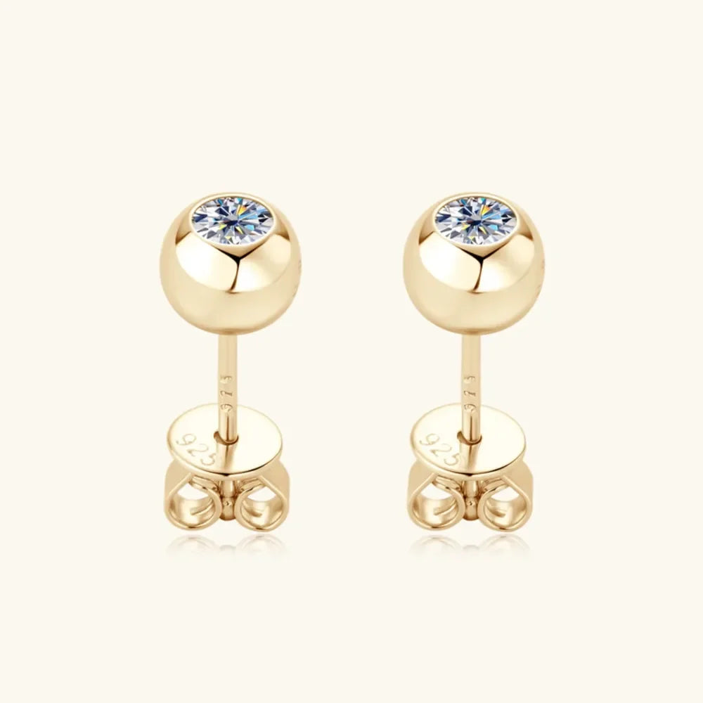 Gold stud earrings with round clear gemstones on a neutral background