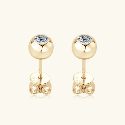 Gold stud earrings with round clear gemstones on a neutral background