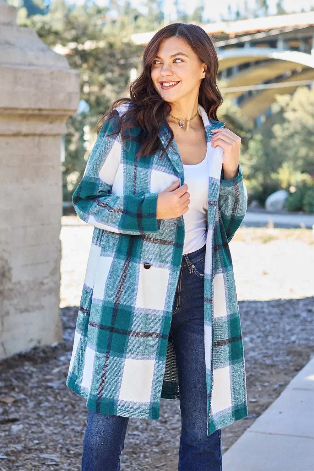 Woman wearing a teal plaid long coat over white top and jeans outdoors