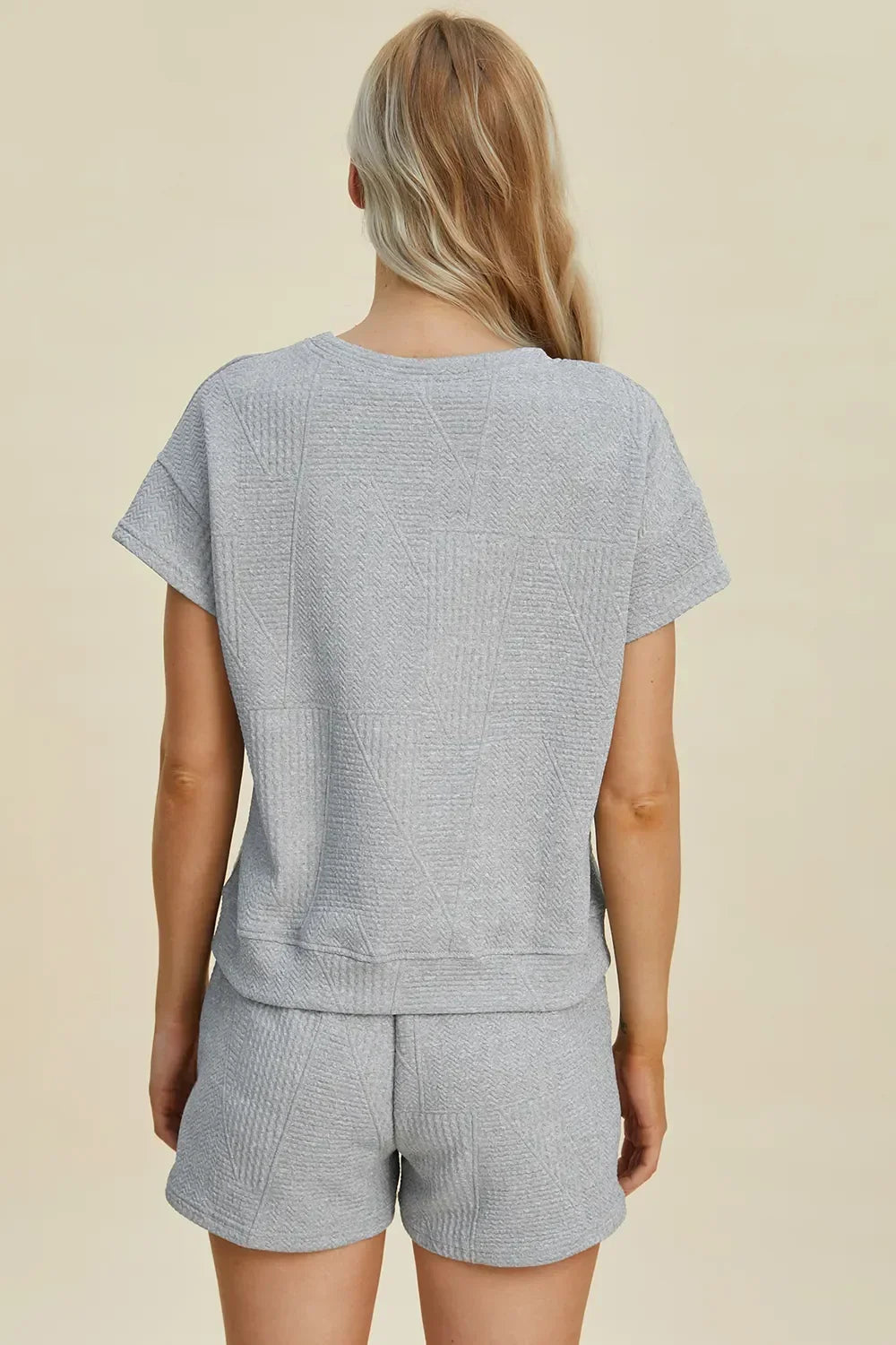 Back view of woman wearing light grey textured short-sleeve lounge set and shorts.