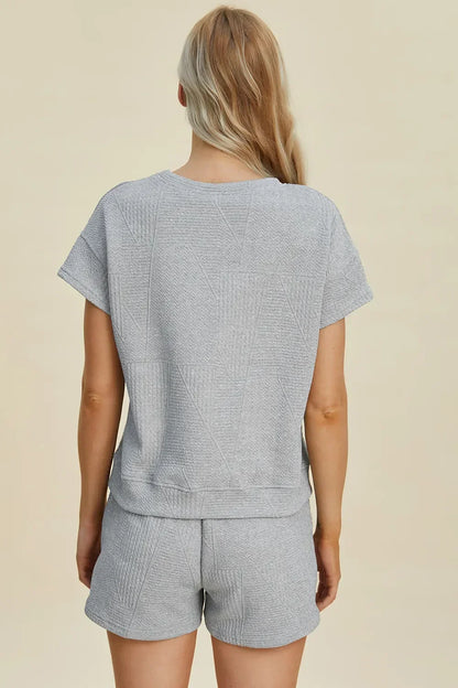 Back view of woman wearing light grey textured short-sleeve lounge set and shorts.