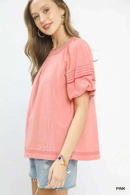 Woman wearing relaxed pink short sleeve blouse with detailing and denim shorts