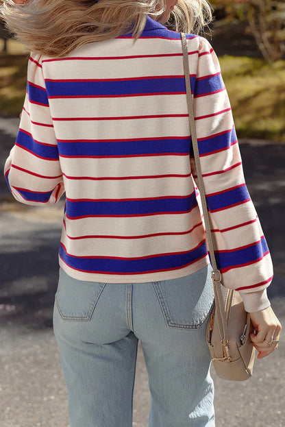 Back view of woman in cream sweater with blue and red stripes, light wash jeans, crossbody bag