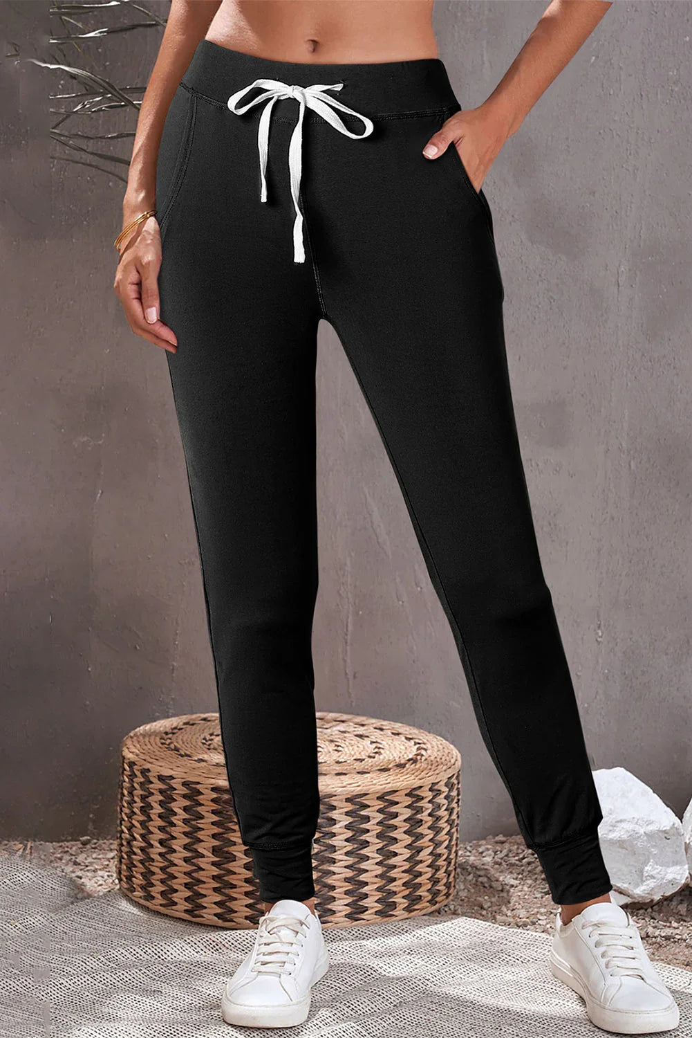 Woman wearing black jogger pants with white drawstring and white sneakers in a casual setting.