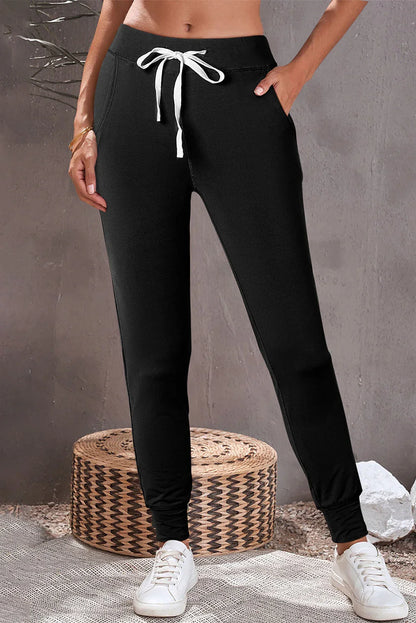 Woman wearing black jogger pants with white drawstring and white sneakers in a casual setting.