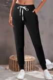 Woman wearing black jogger pants with white drawstring and white sneakers in a casual setting.