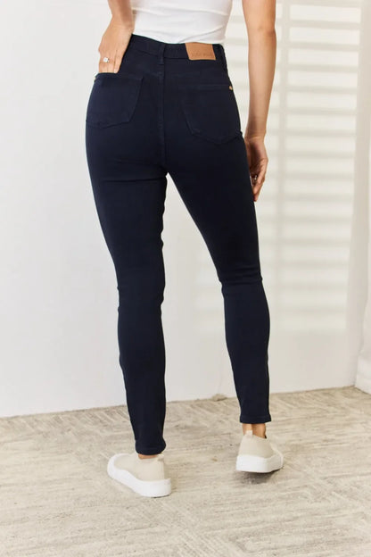 Woman wearing dark skinny jeans and white top, shown from the back, in a bright room