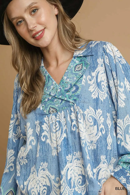 Woman wearing a blue and white floral boho blouse with green embroidered neckline and black hat