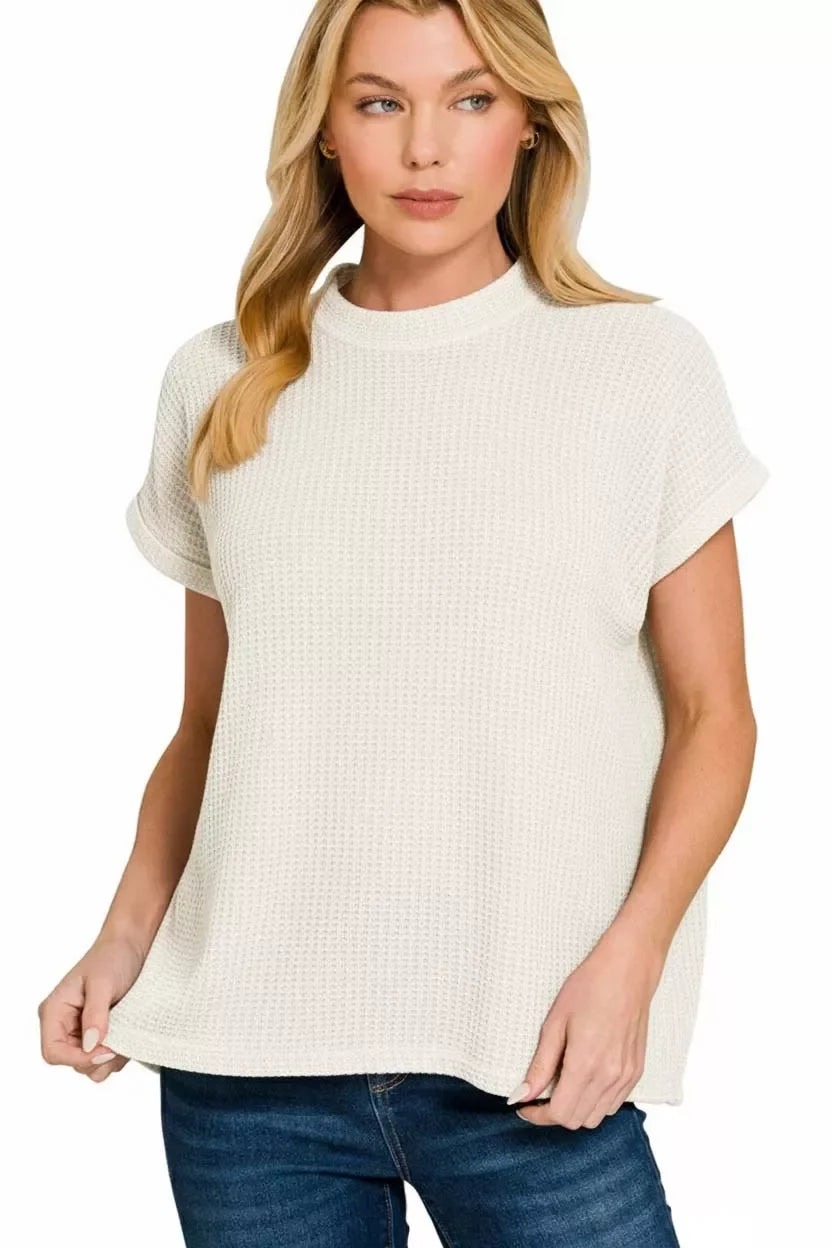 Woman wearing a short sleeve white textured knit top with rolled cuffs and blue jeans