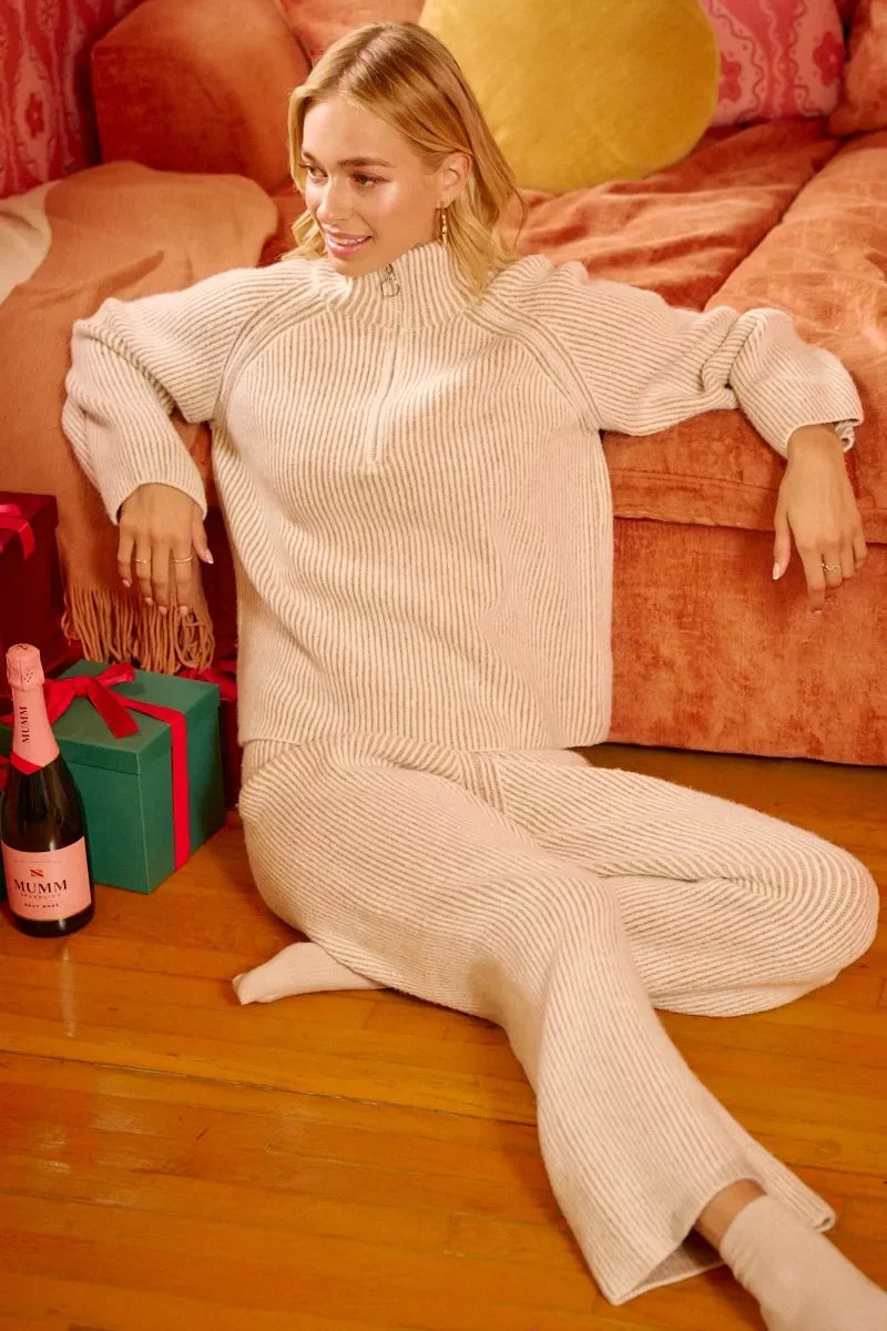 Woman in cozy cream ribbed knit loungewear sitting by coral sofa with gifts and champagne