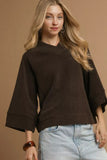 Woman wearing a loose-fit chocolate brown top with wide sleeves and light wash denim jeans