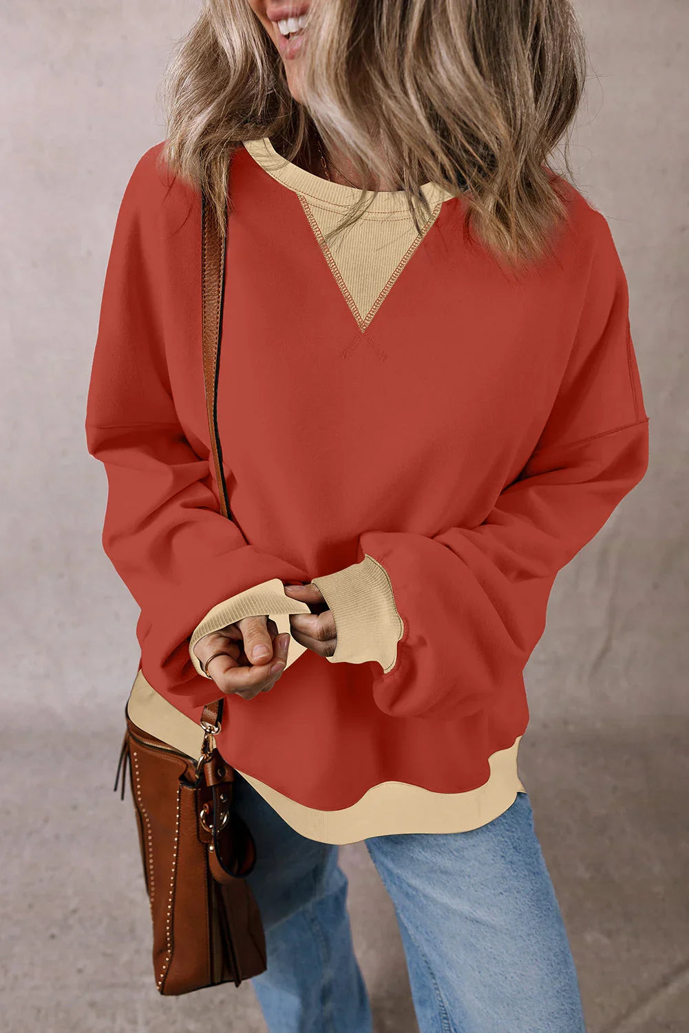 Woman in oversized colorblock sweatshirt with beige accents, jeans, and brown bag