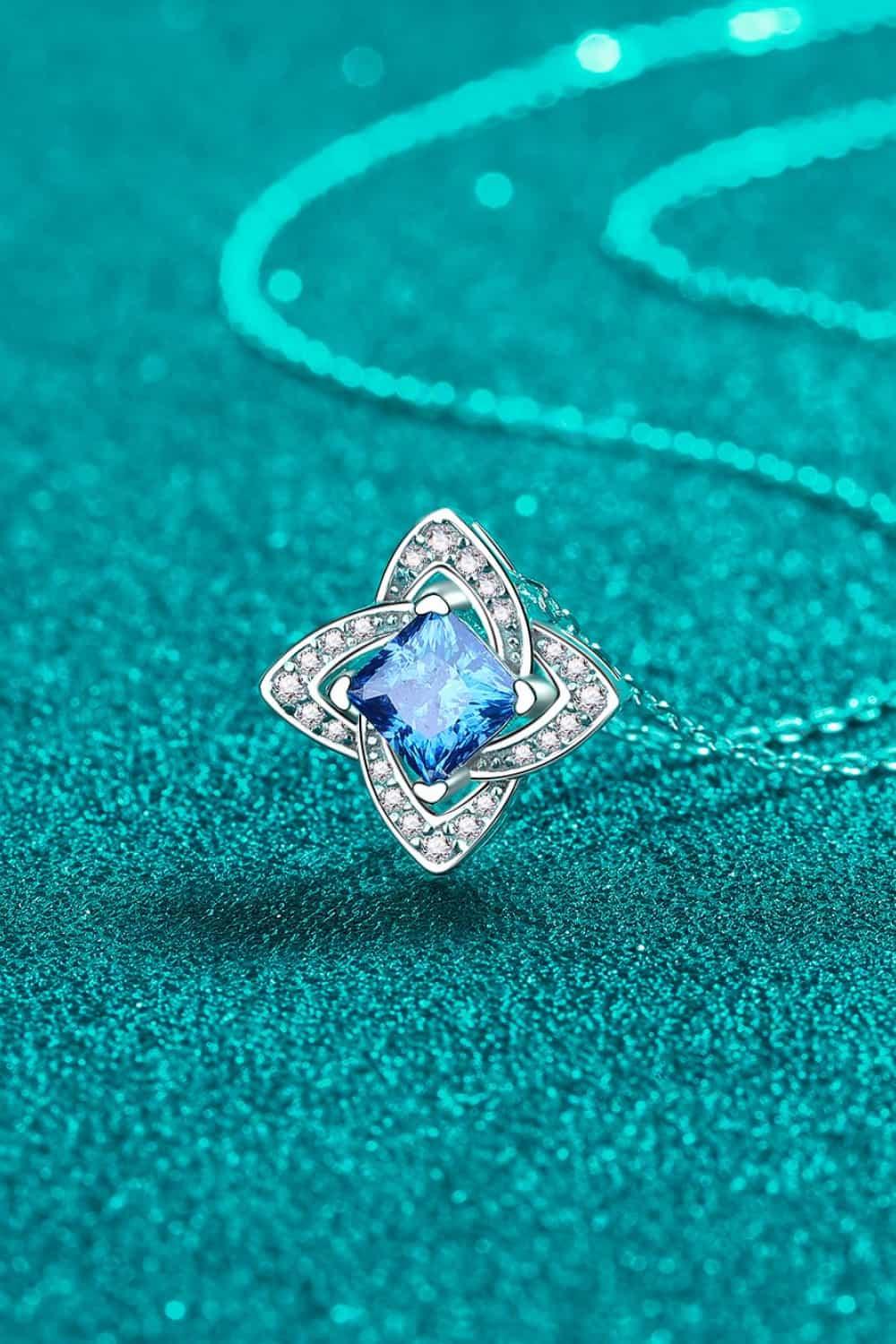 Silver necklace with blue gemstone and diamond-like accents on textured teal background