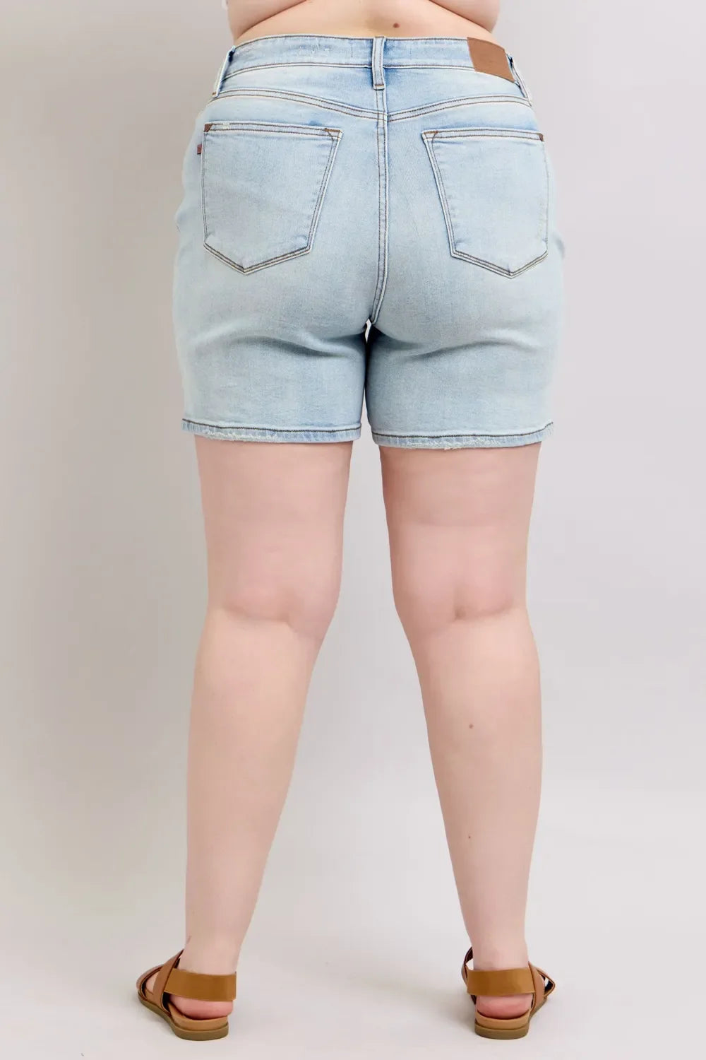 Back view of a woman wearing light wash denim shorts and brown sandals.