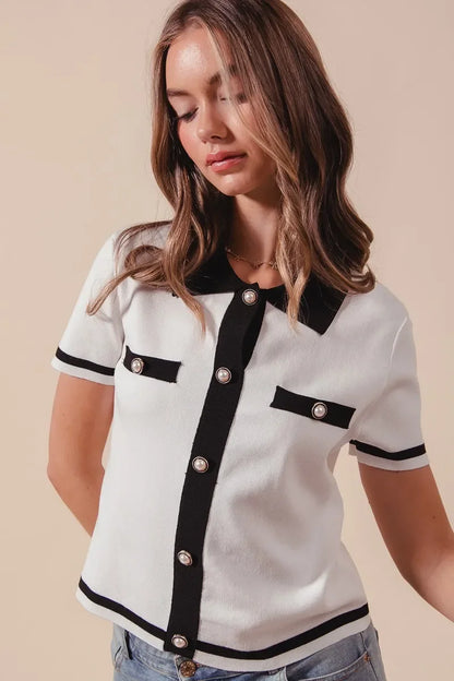 Woman wearing a short sleeve white knit top with black trim and pearl buttons