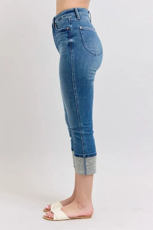 Woman wearing cropped blue cuffed jeans and white slide sandals on a light background