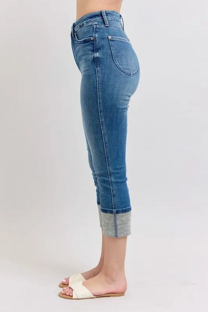 Woman wearing cropped blue cuffed jeans and white slide sandals on a light background