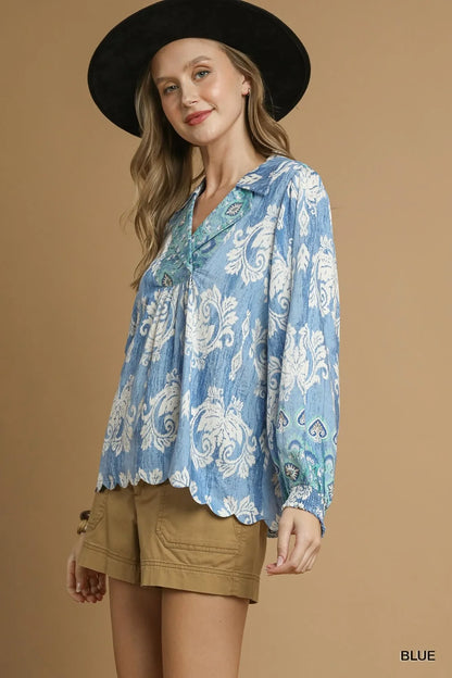 Woman wearing a flowy blue patterned blouse with long sleeves and tan shorts.