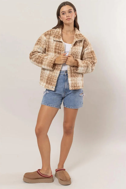 Woman wearing a beige plaid textured jacket, denim shorts, and tan slip-on shoes