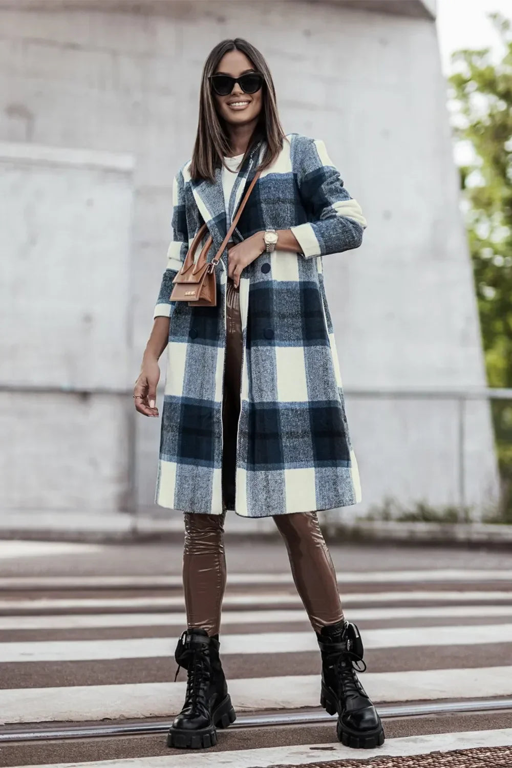Woman wearing long plaid coat, faux leather leggings, and black combat boots outdoors