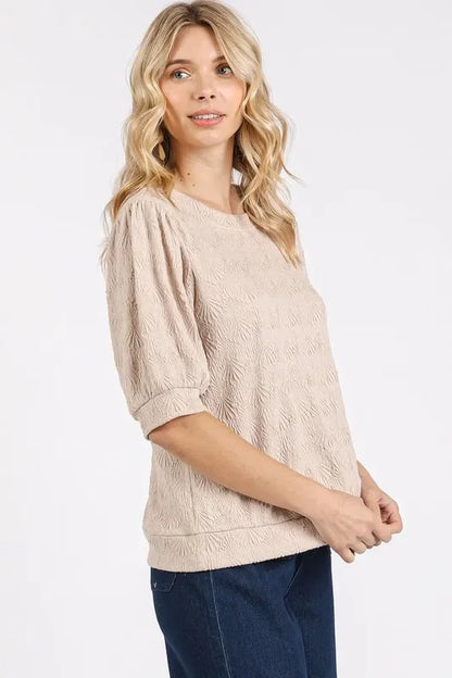 Woman wearing a textured beige short-sleeve blouse with relaxed fit and dark jeans