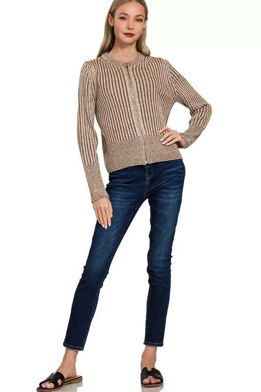 Woman wearing a beige ribbed zip-up sweater, dark skinny jeans, and black sandals on white background.