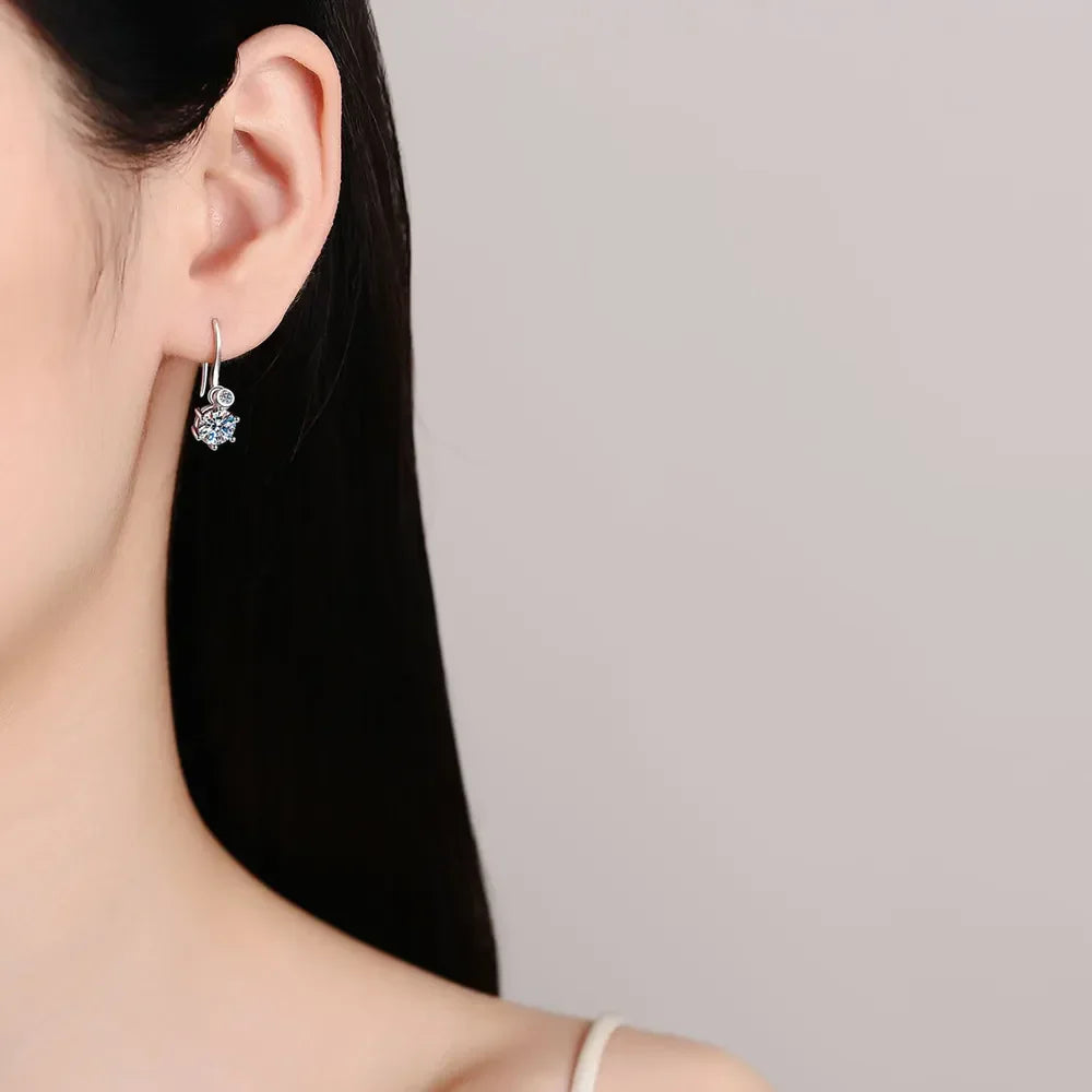 Elegant silver hoop earring with crystal floral charm on woman's ear, minimal background