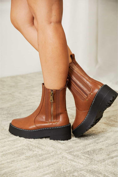Brown leather platform ankle boots with side zippers and chunky soles on a textured rug