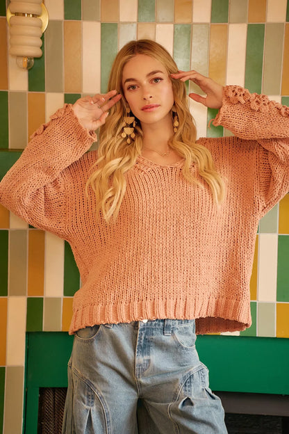 Woman wearing a loose peach knit sweater and relaxed blue jeans, standing indoors.