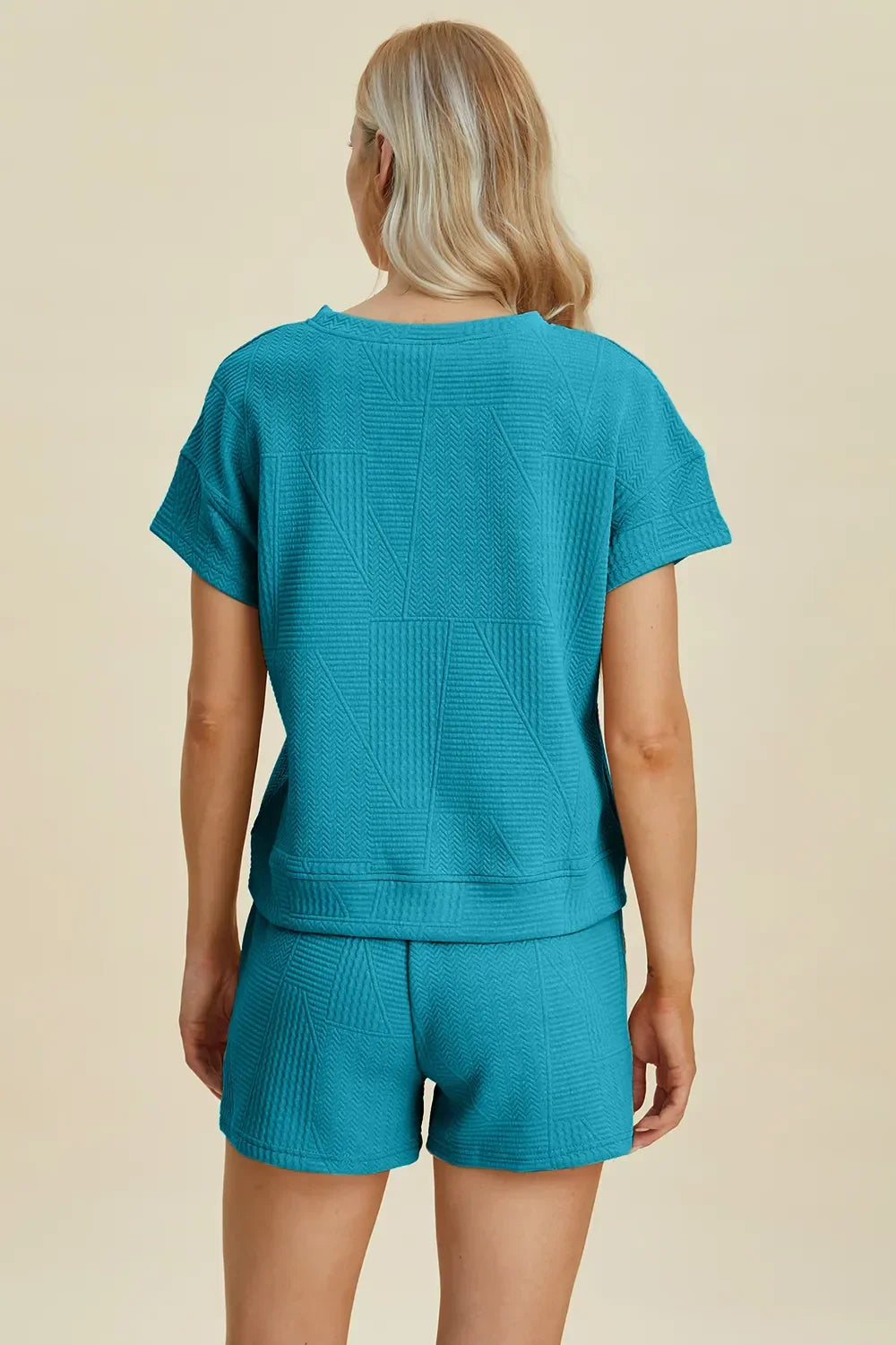 Woman wearing a textured turquoise short-sleeve top and matching shorts set, back view