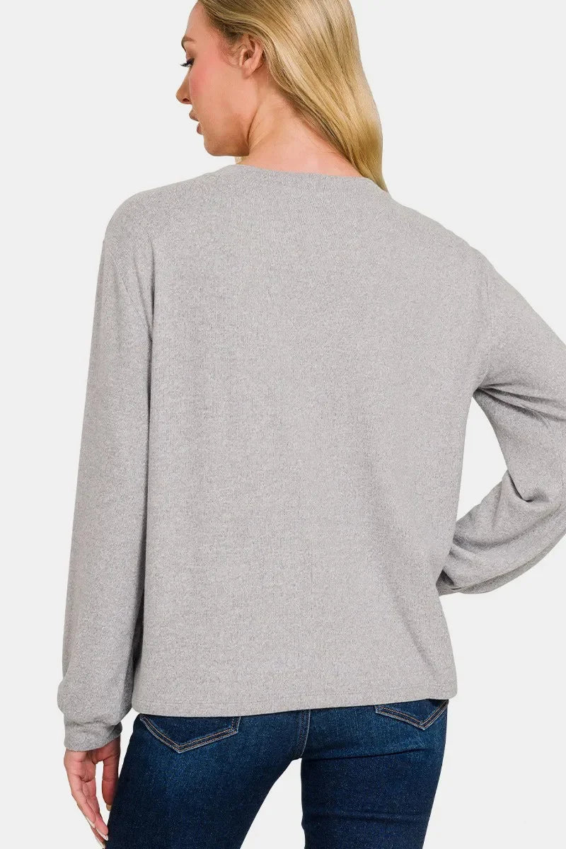 Woman wearing a light grey long sleeve knit top with relaxed fit and blue jeans, back view