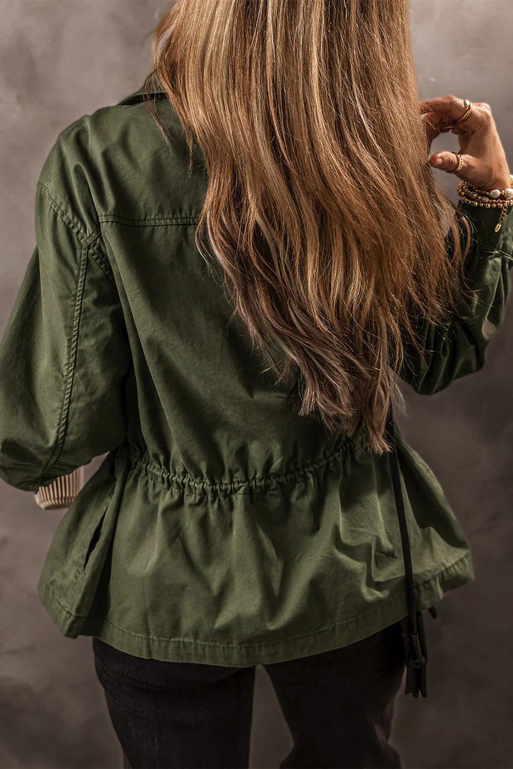 Woman wearing an olive green utility jacket with cinched waist, shown from the back