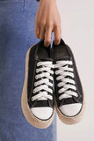 Hand holding black canvas sneakers with white laces and woven platform soles