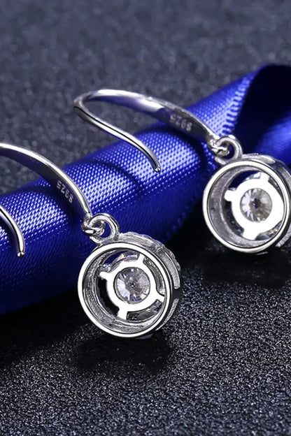 Sterling silver dangle earrings with round cubic zirconia stones on a textured surface.