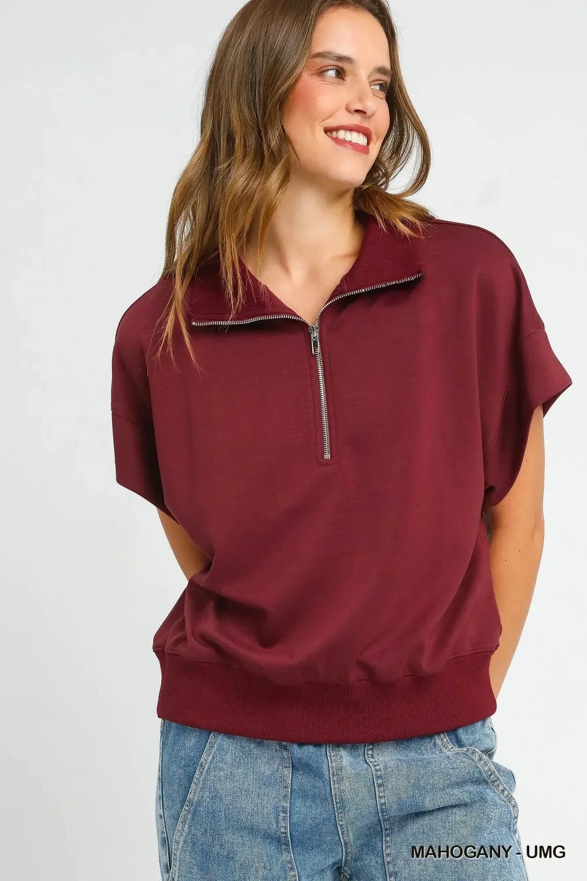 Woman wearing a relaxed fit mahogany short sleeve zip collar top with blue denim jeans.