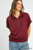 Woman wearing a relaxed fit mahogany short sleeve zip collar top with blue denim jeans.