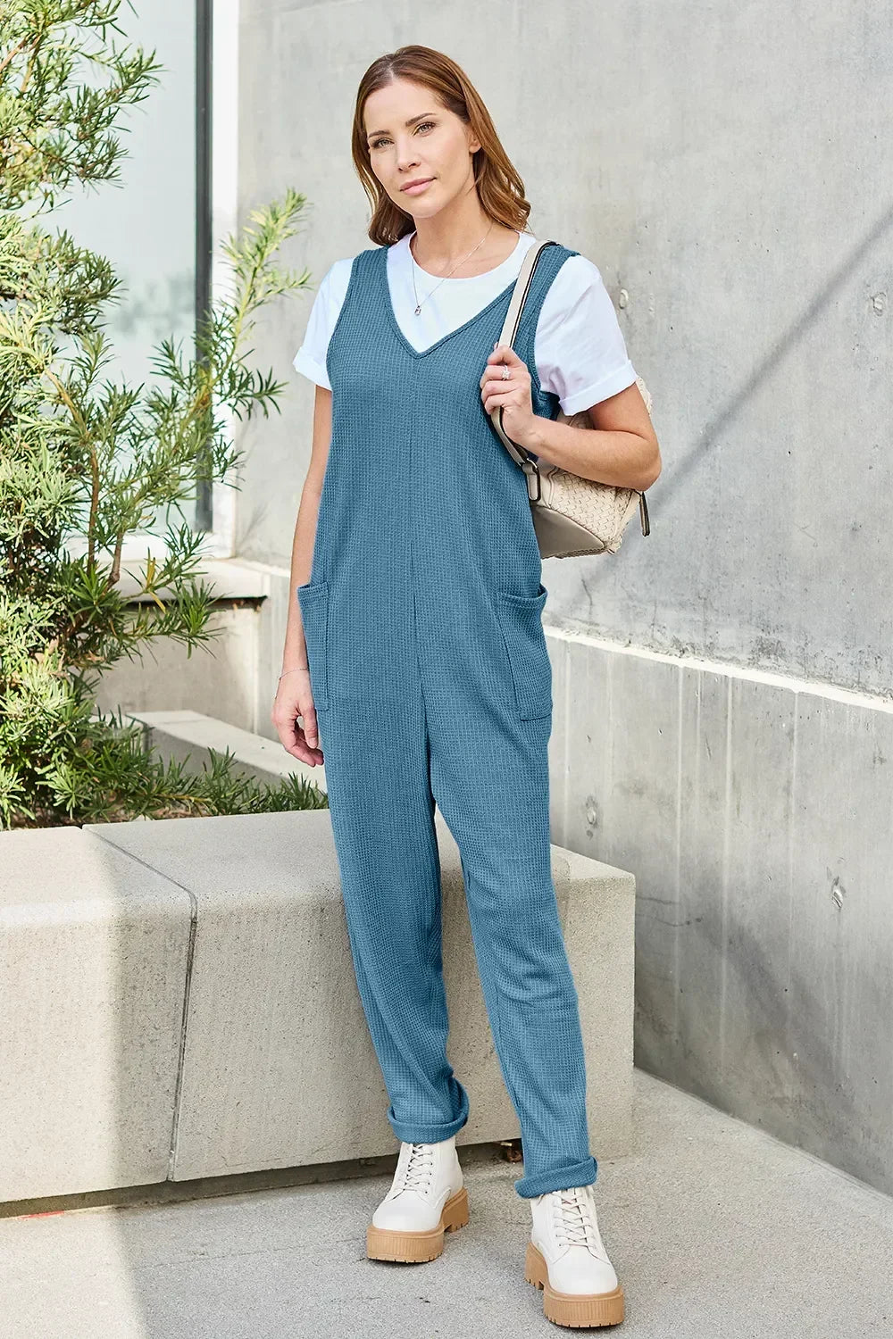 Woman wearing relaxed blue jumpsuit over white t-shirt, casual boots, outdoor setting