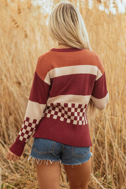 Woman in striped and checkered knit sweater with denim shorts standing in tall grass