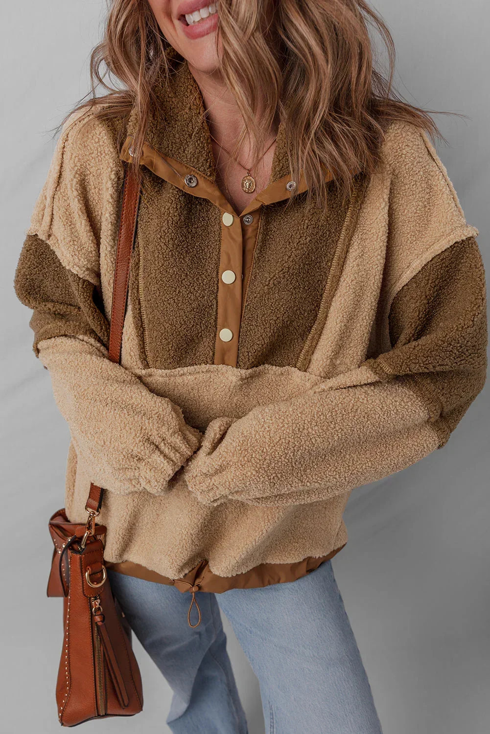 Woman wearing a cozy two-tone sherpa pullover, light wash jeans, and carrying a brown leather bag.
