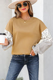 Woman in tan oversized sweatshirt with floral and striped sleeves, jeans, and sun hat