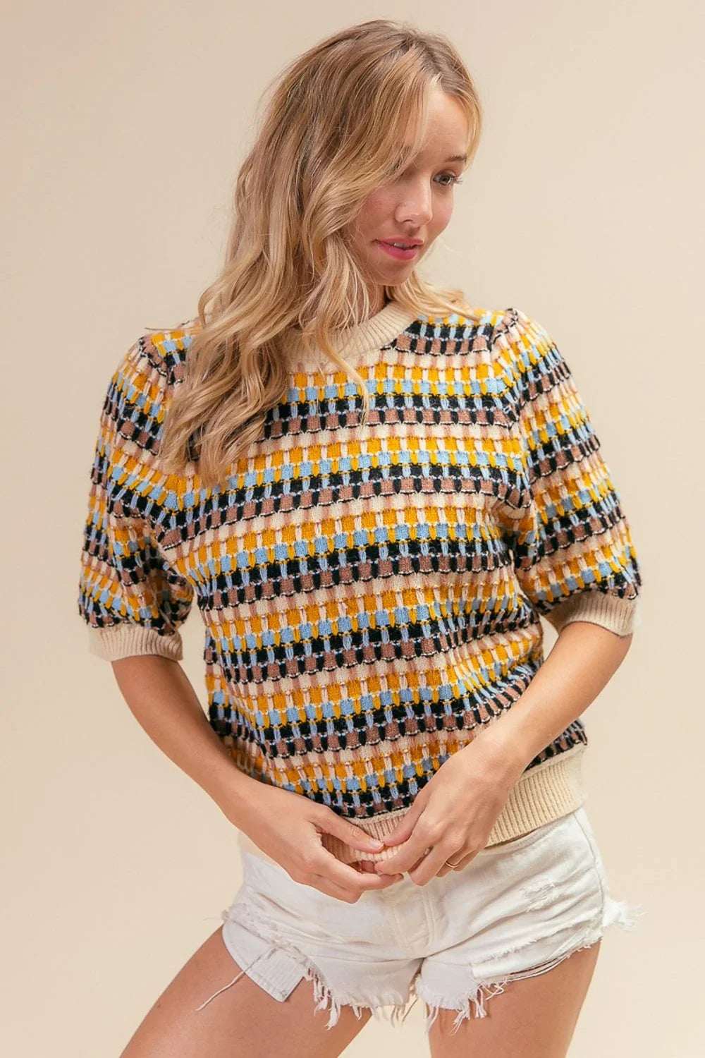 Woman wearing a colorful textured knit sweater with short sleeves and distressed white shorts