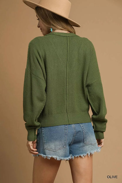 Woman in olive green textured sweater, denim shorts, and tan hat, shown from the back.