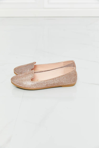 Rose gold rhinestone loafers with flat sole on white marble floor