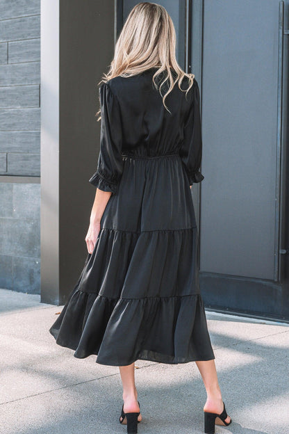 Woman wearing a black tiered midi dress with three-quarter sleeves and block heel sandals