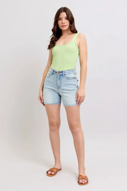 Woman wearing light green tank top, light wash high-waisted denim shorts, and tan sandals