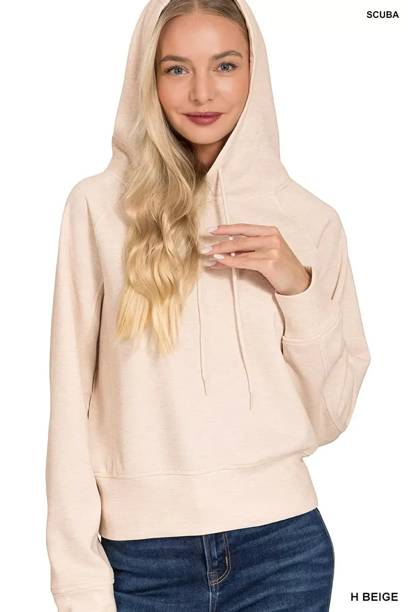 Woman wearing a beige hooded sweatshirt with drawstrings and blue jeans, front view.