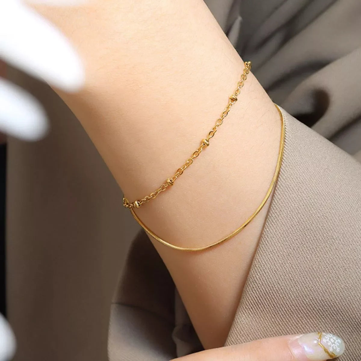 Woman wearing delicate gold chain bracelets on wrist, dressed in neutral-toned clothing
