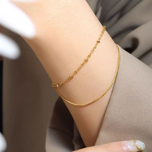 Woman wearing delicate gold chain bracelets on wrist, dressed in neutral-toned clothing