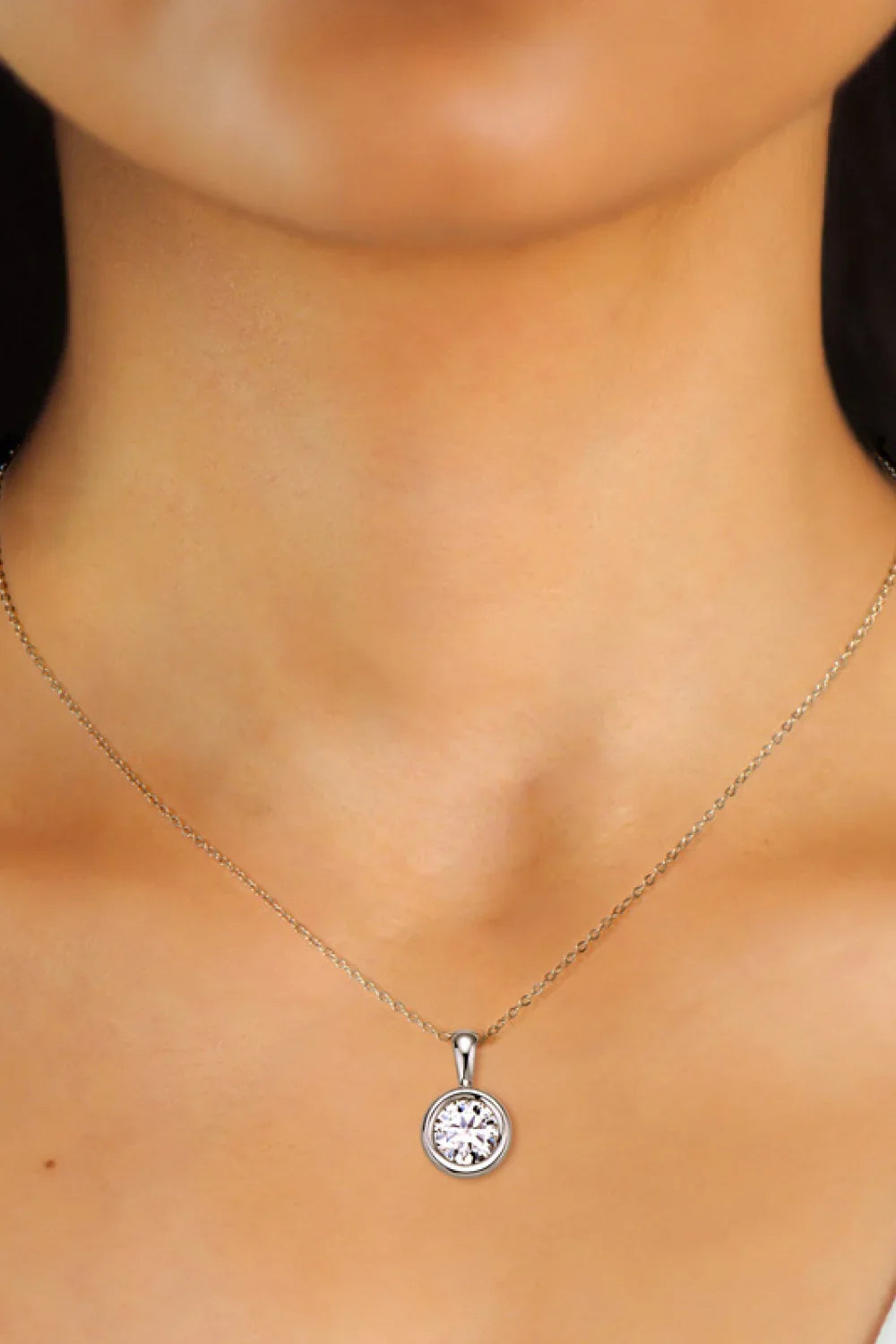 Delicate silver necklace with round solitaire pendant on woman's neck, minimalist jewelry